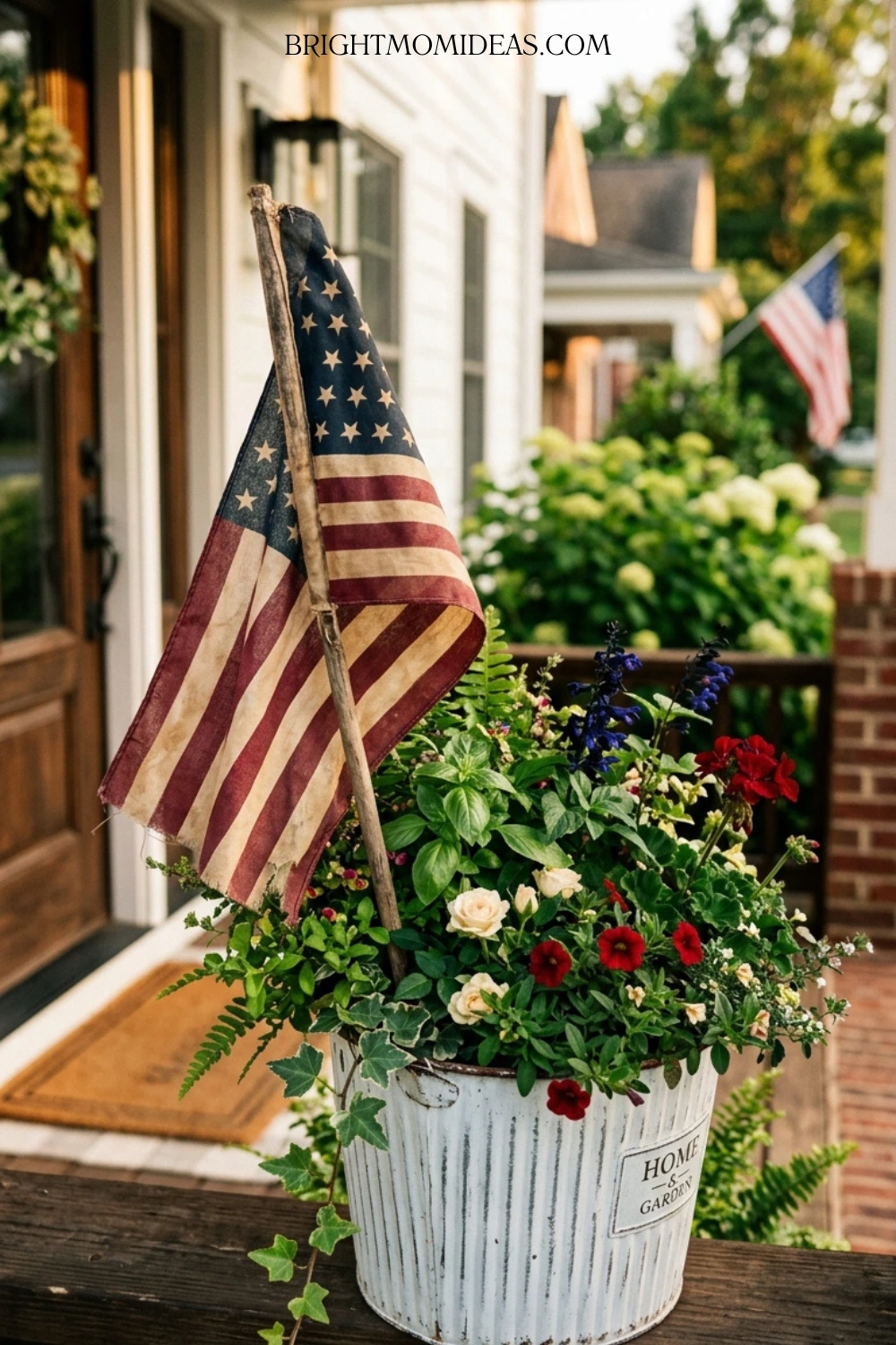 White galvanized planter with greenery red petunias 
and single small American stick flag tucked naturally 
among the blooms