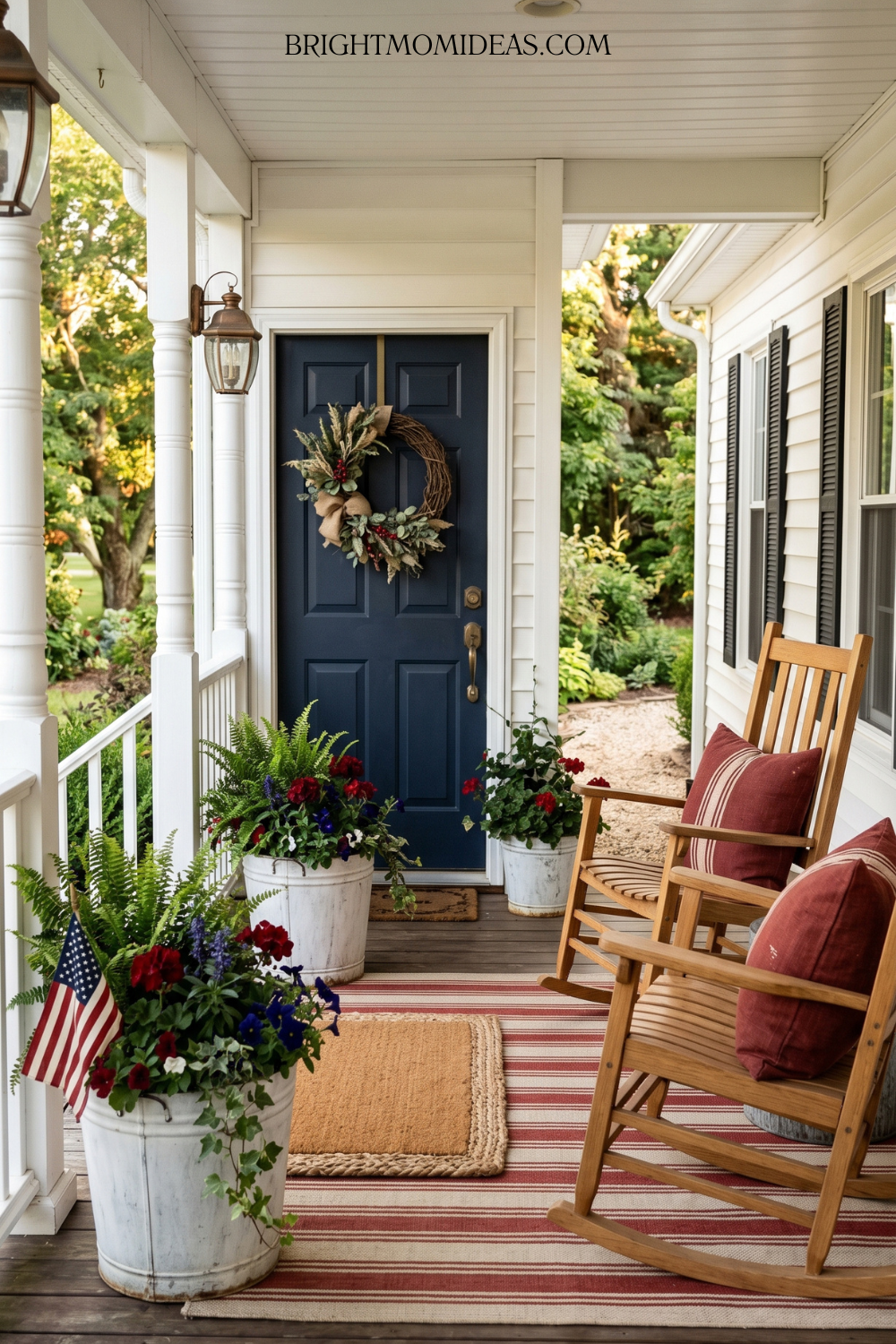 Classic Americana front porch with wood rocking chairs grain sack red pillows striped rug and galvanized planters with red and blue flowers