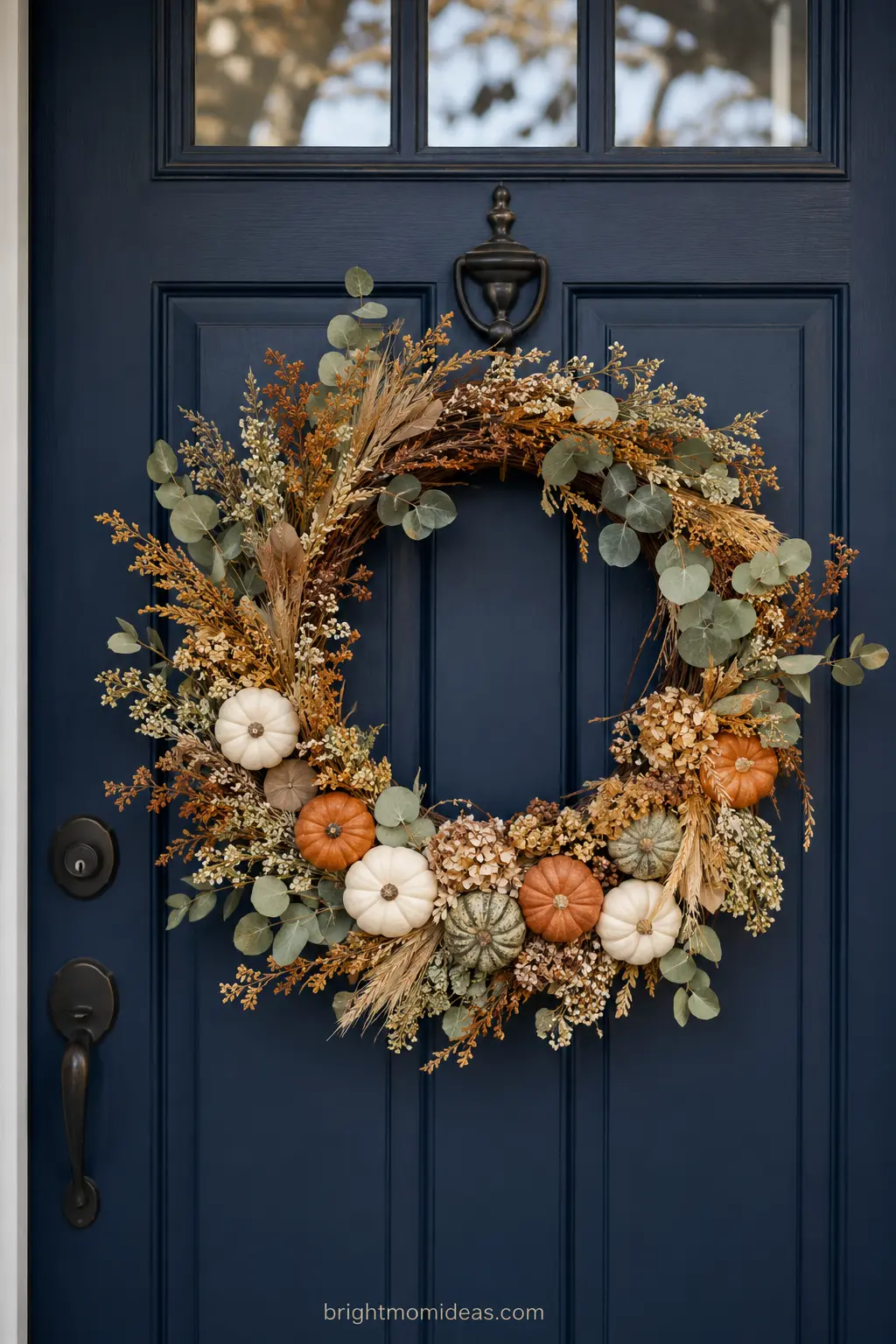 Dried floral and eucalyptus wreath with mini pumpkins on front door